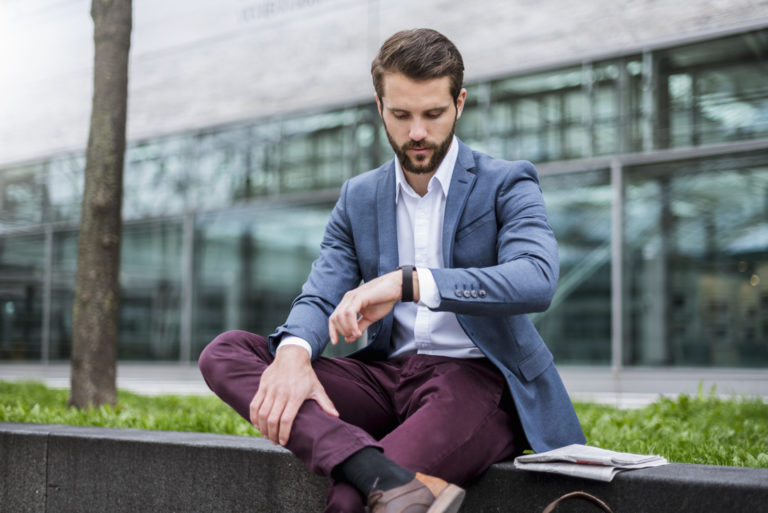 Young businessman sitting outdoors checking the time